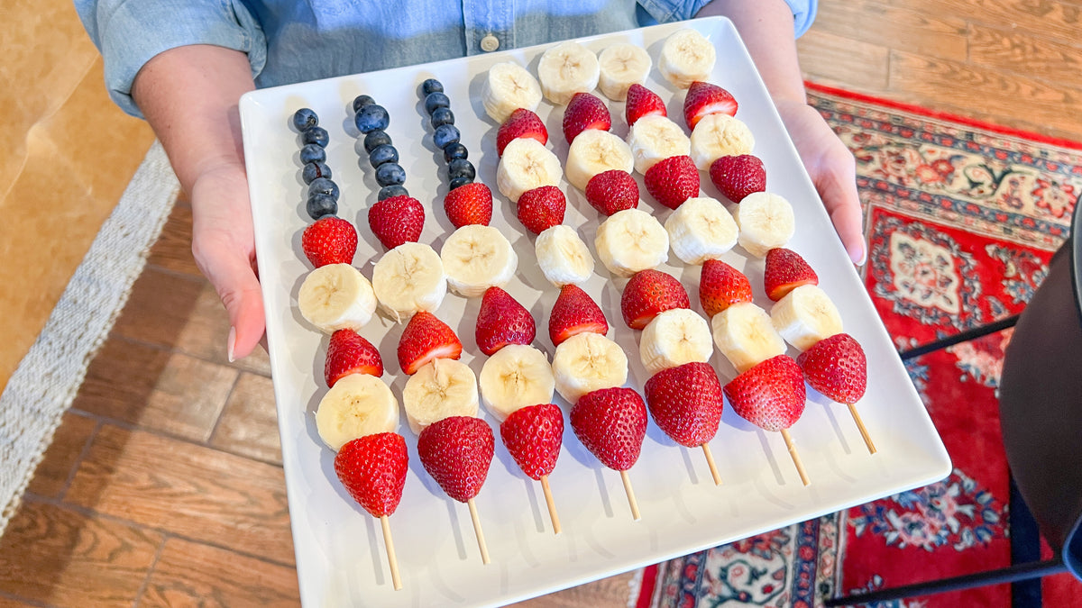 A woman in a blue denim shirt holds a tray of patriotic fruit skewers for the 4th of July