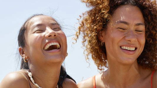 Two women laughing outside under a blue sky